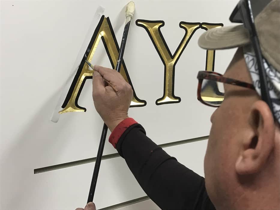 Image of a painter pinstriping around a gold leaf letter on a sign face